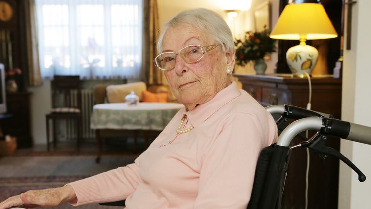 Seniorin sitzt in ihrem Zimmer im Rollstuhl