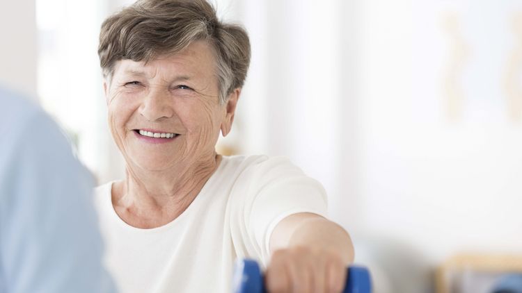 Seniorin übt mit kleinen blauben Hanteln