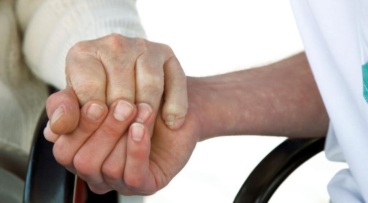 Pflegerin hält Hand eines älteren Bewohners