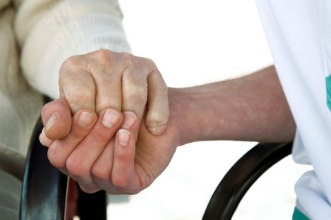 Pflegerin hält Hand eines älteren Bewohners