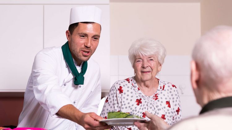 Koch serviert Seniorin eine Mahltzeit