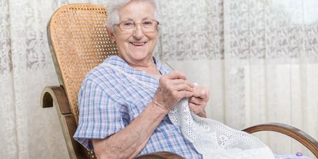 Ältere Frau sitzt im Schaukelstuhl und häkelt